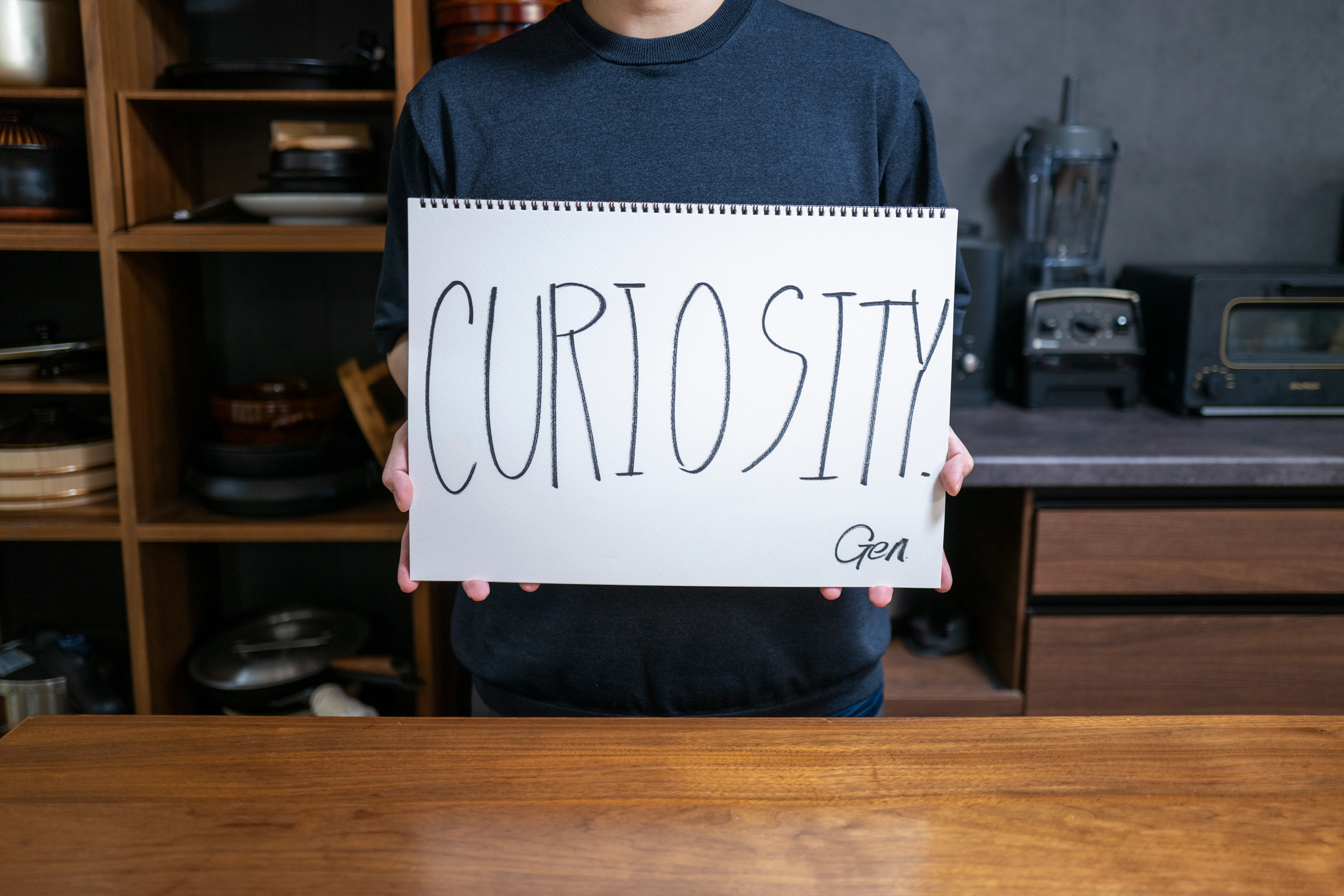 CURIOSITYと書かれたフリップをもつGenさん