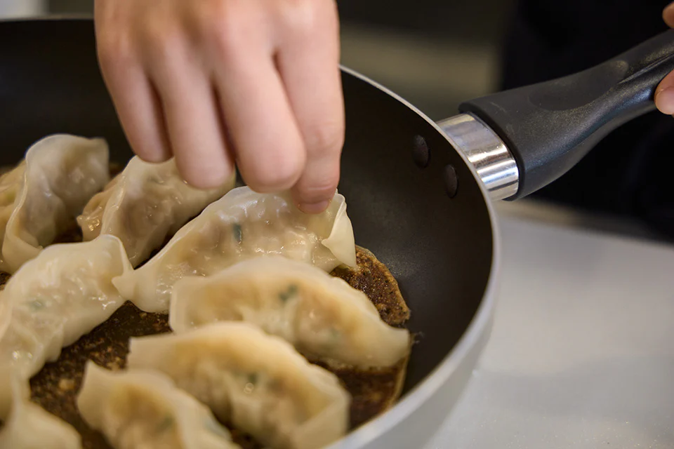 焼き加減を確認するため、フライパンの中の「ギョーザ」の端を指で優しく持ち上げている手元