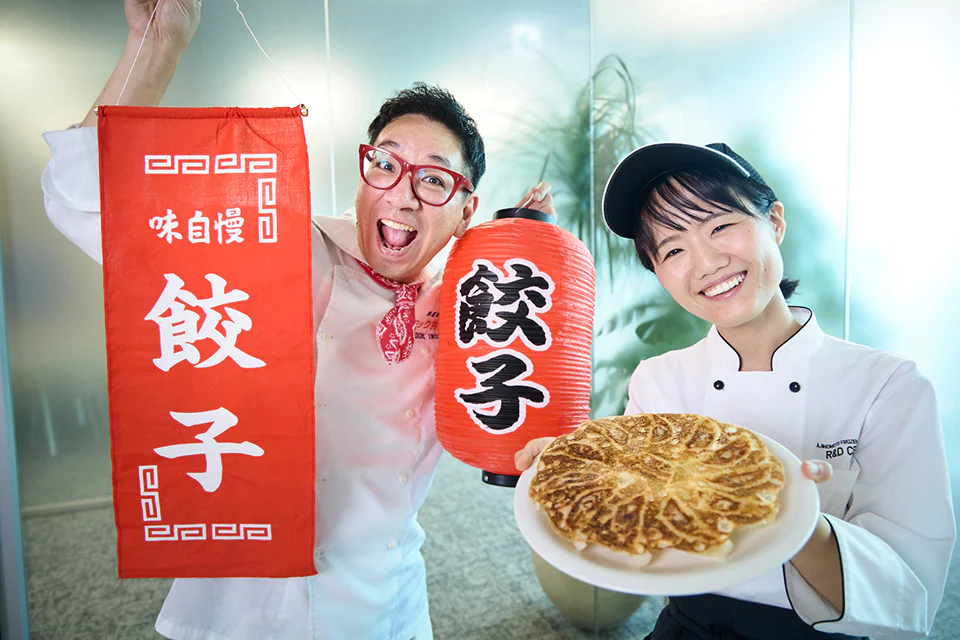 餃子グッズを持って盛り上げるクック。井上さんと、焼き上がった「ギョーザ」の皿を持ち笑顔の竹内さん