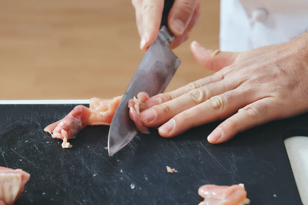 鶏肉をそぎ切りにする際は、皮目を下にし、寝かせた包丁の刃元を肉に当てる