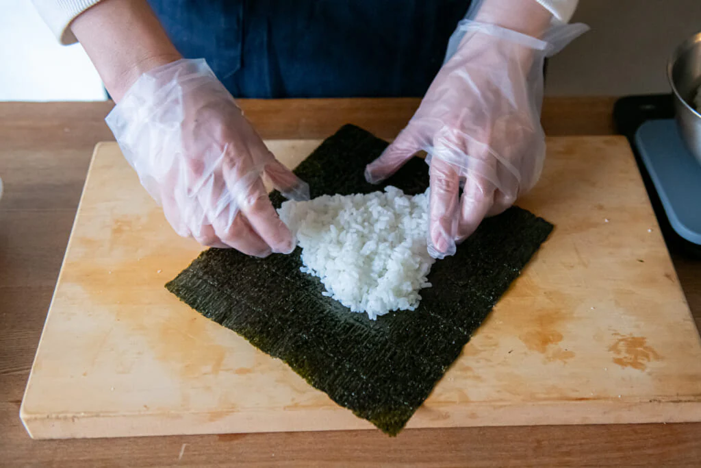 のりをひし形におき、中央にごはんの1/2量を三角形になるようにのせる。