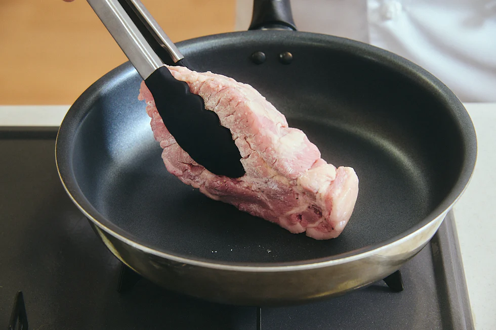 フライパンに肉を入れる様子