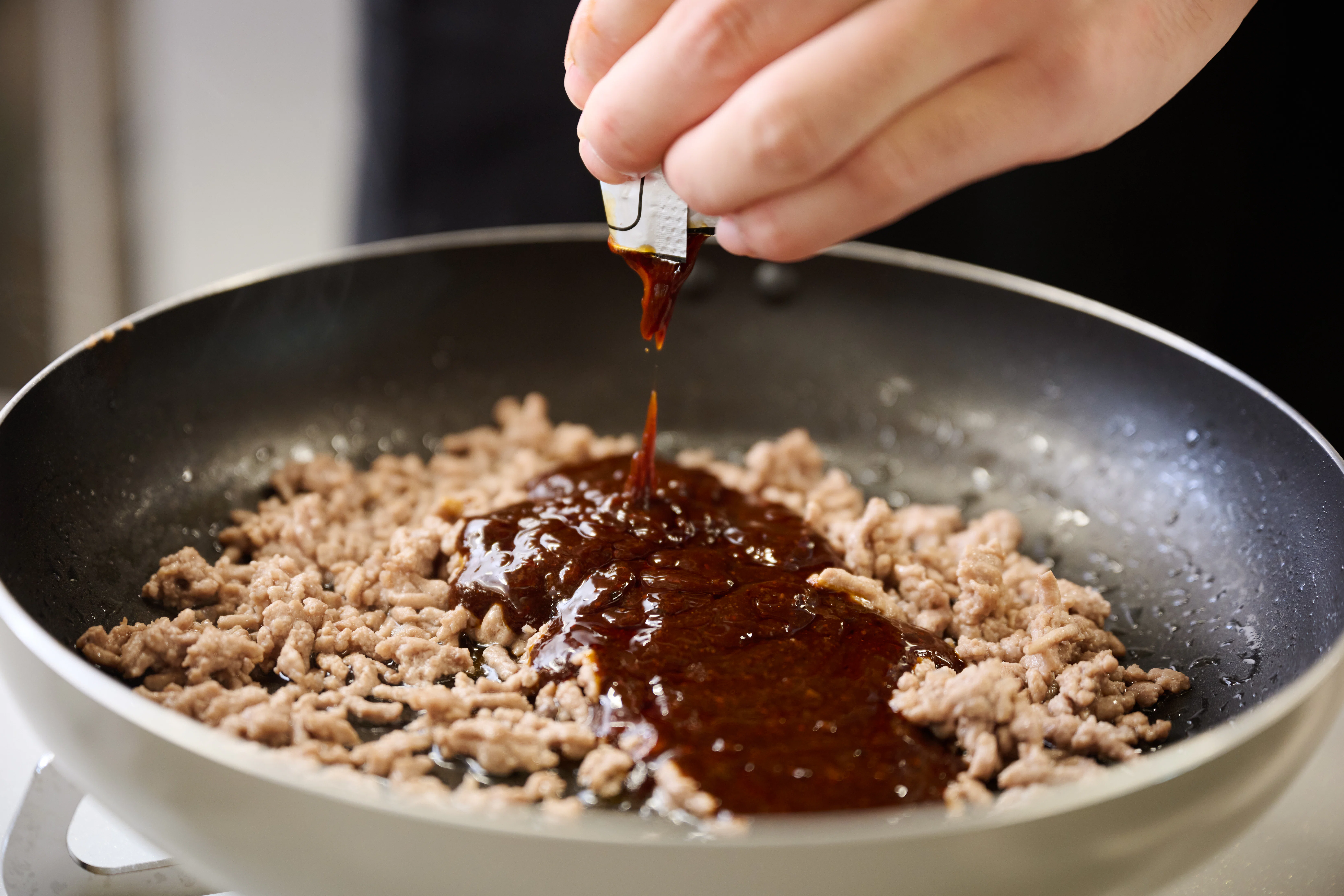 ひき肉を炒めたフライパンに「Cook Do®」<極 華辣麻婆豆腐用>のソースをかける様子