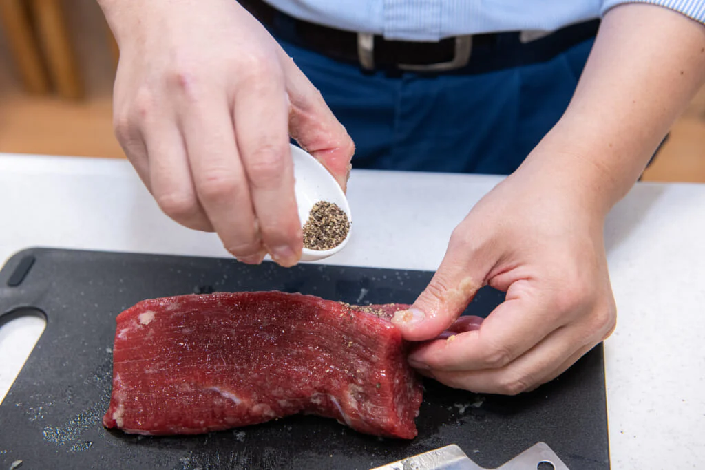 冷蔵庫から出した牛モモ肉ブロックに塩、おろしにんにく、黒こしょうを手で擦り込みます