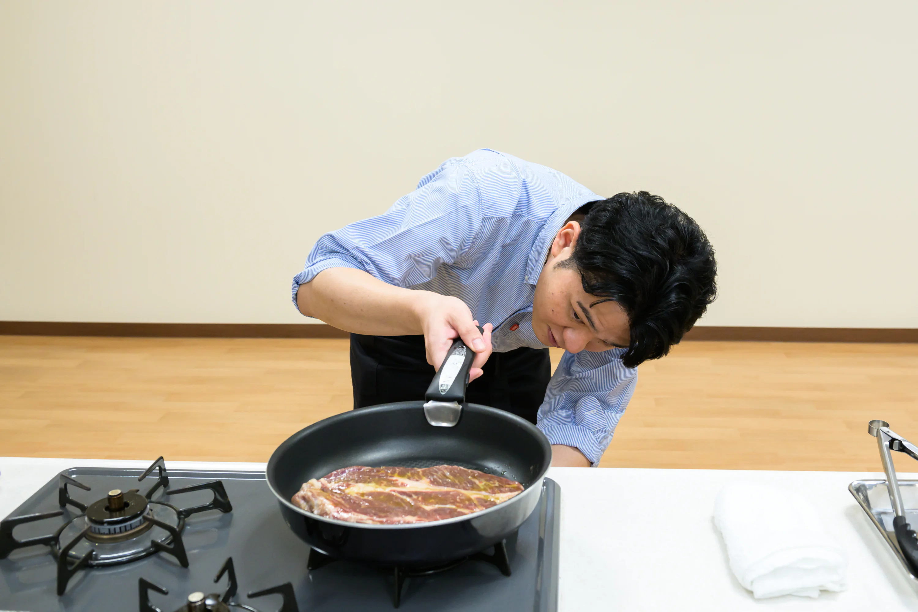 肉が入ったフライパンとコンロに火をつける木場さん