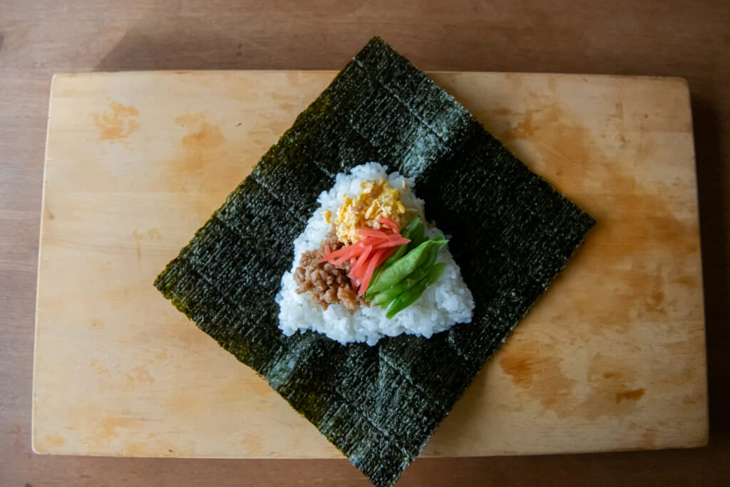 ごはんの真ん中に、卵そぼろと鶏そぼろの半量、いんげん、紅しょうがをのせ、残りのごはんをかぶせる。