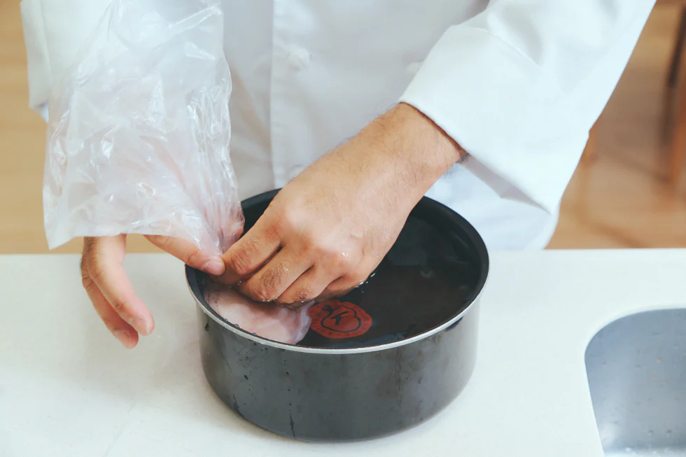 胸肉に液をもみこんだら、全体にムラなく酒と塩を浸透させるため、袋の空気を抜きます。鍋やボウルに水をはり、袋の口を水面より上に出すようにして入れると、水圧で簡単に空気が抜けます。それから口をしっかりとじてください