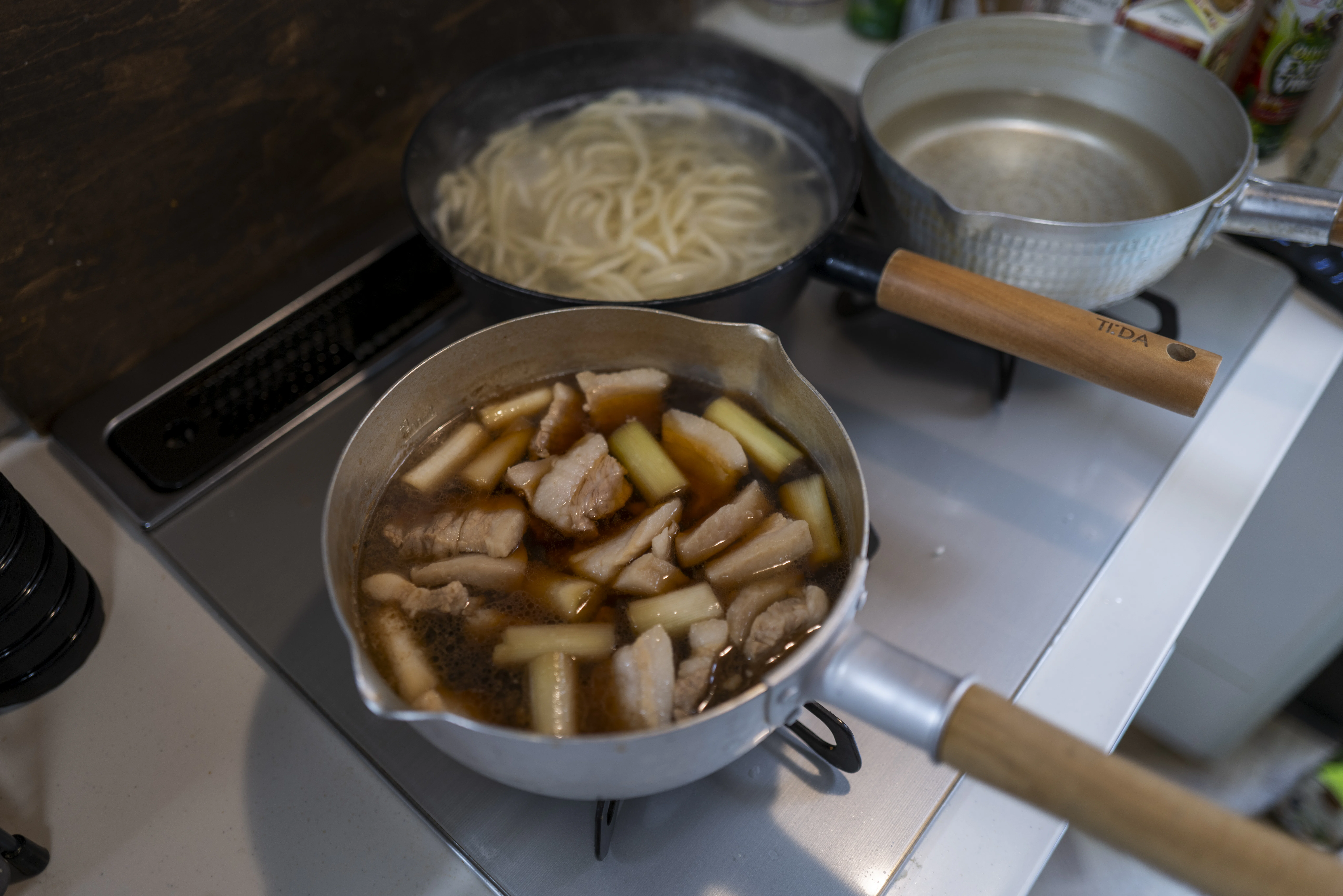 下ゆでした豚バラ肉とネギがうどんのつゆと共にお鍋に入って調理されている様子