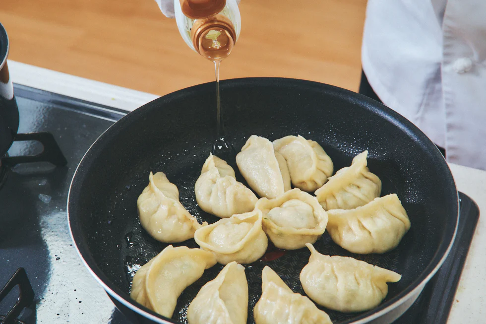 餃子の入ったフライパンに油をいれている