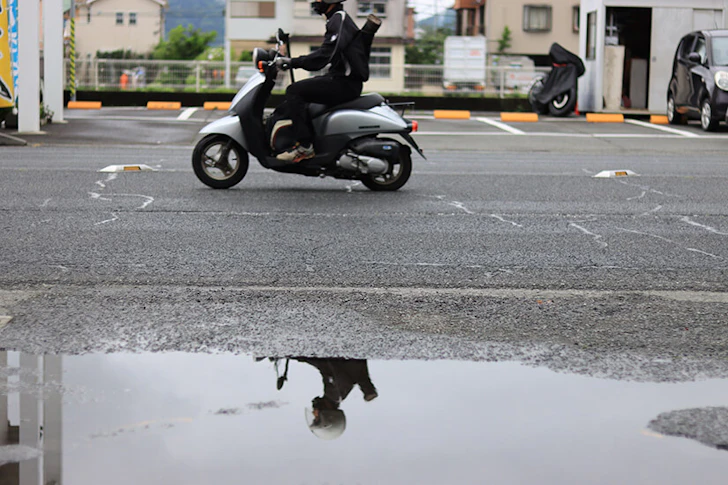バイク走行中の男性の姿が水たまりに反射している