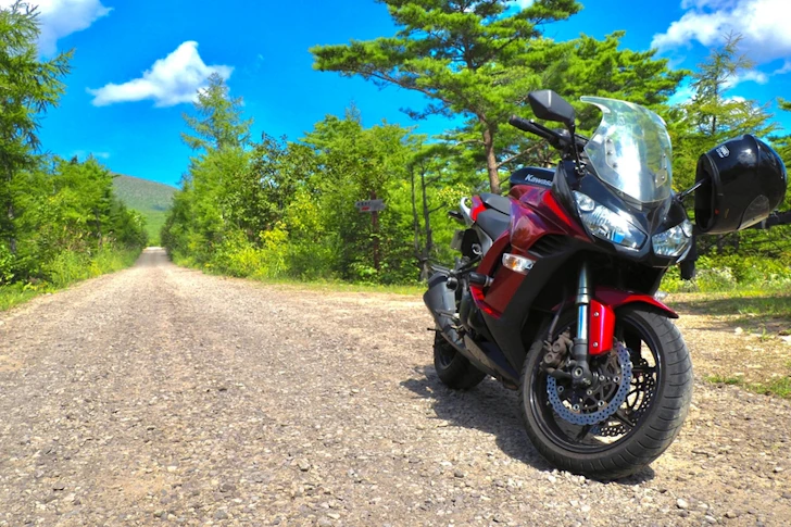 青空と木々を背景に、道に停められた赤いバイク。