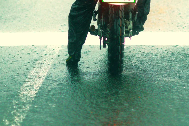 雨のなかでバイクが停止線で停車している様子。