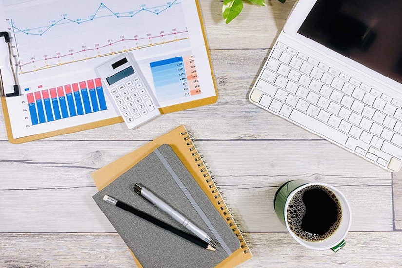 書類やパソコン、ノート、ペン、コーヒーなどがデスクの上に広がっている。