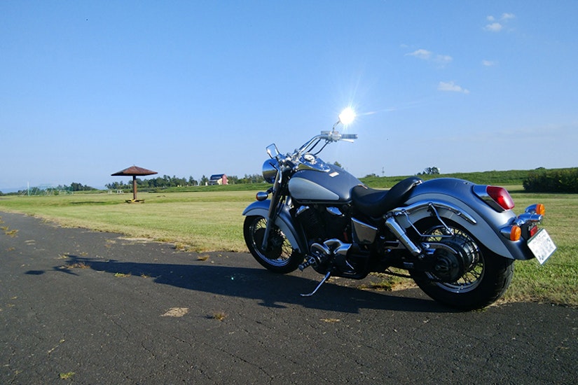 ひらけた公園の脇に停められたバイクのミラーに太陽の光が反射している