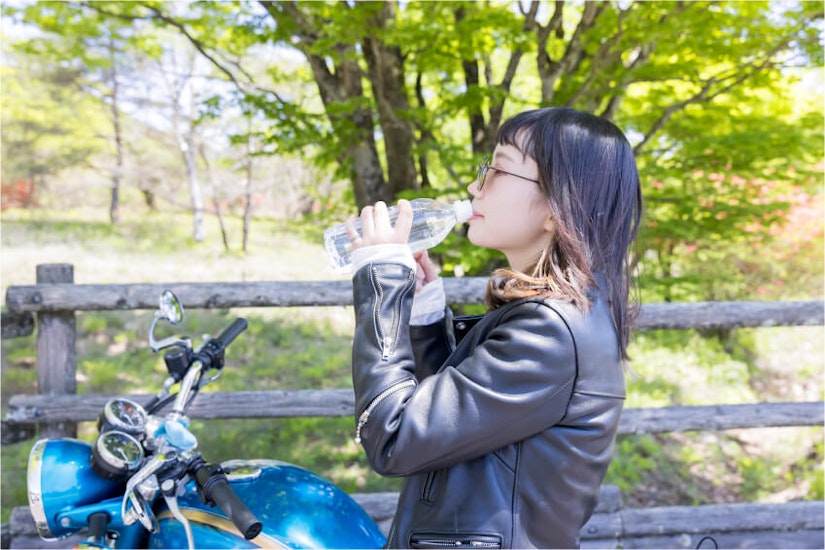 バイクのそばで水を飲む女性