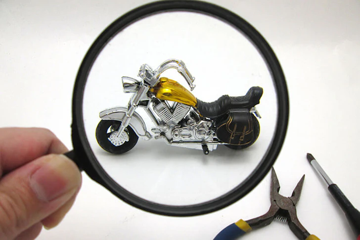 虫眼鏡でバイクのミニチュアを覗いている