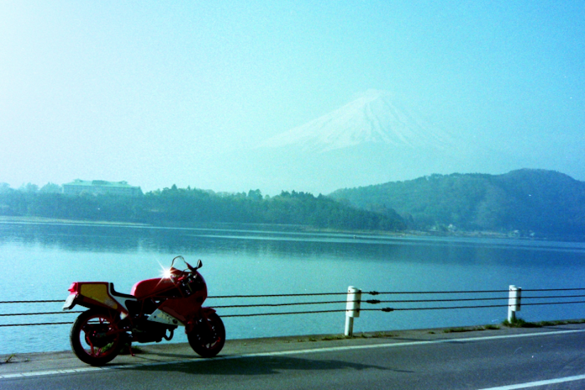 奥に山が見える湖近くの道路にバイクが停まっている