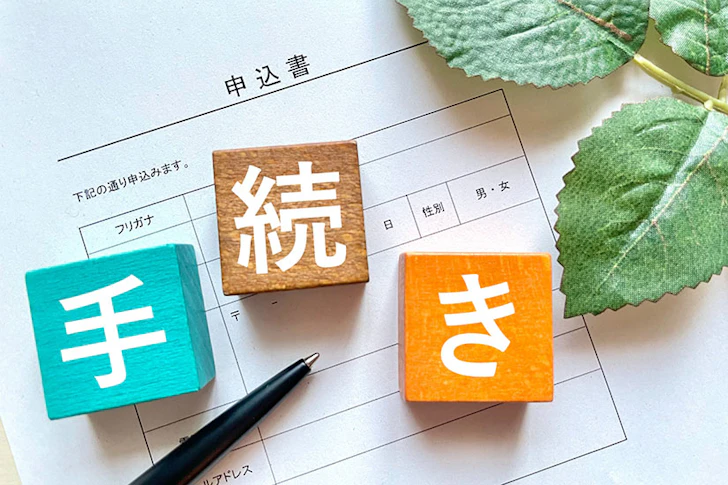 手続きと書かれた木のオブジェと申込書やペン、葉っぱなどが写っている。