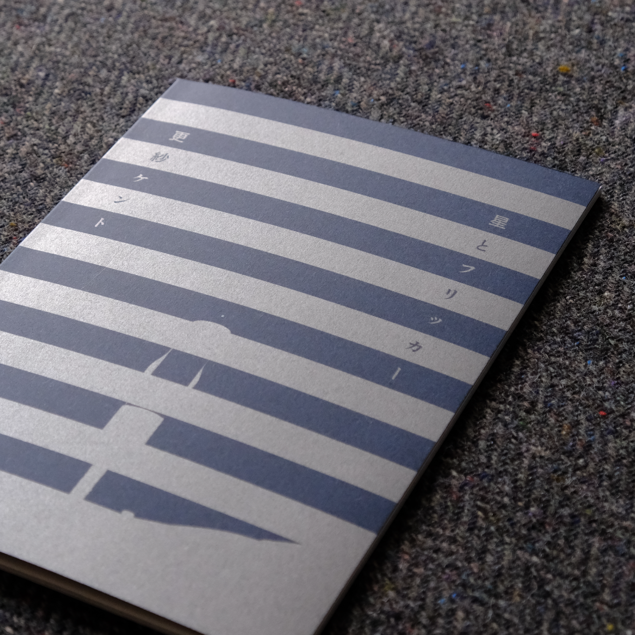 布の上に『星とフリッカー』が表紙を表にして置かれている。銀インクで印刷された部分が光沢をもっている。