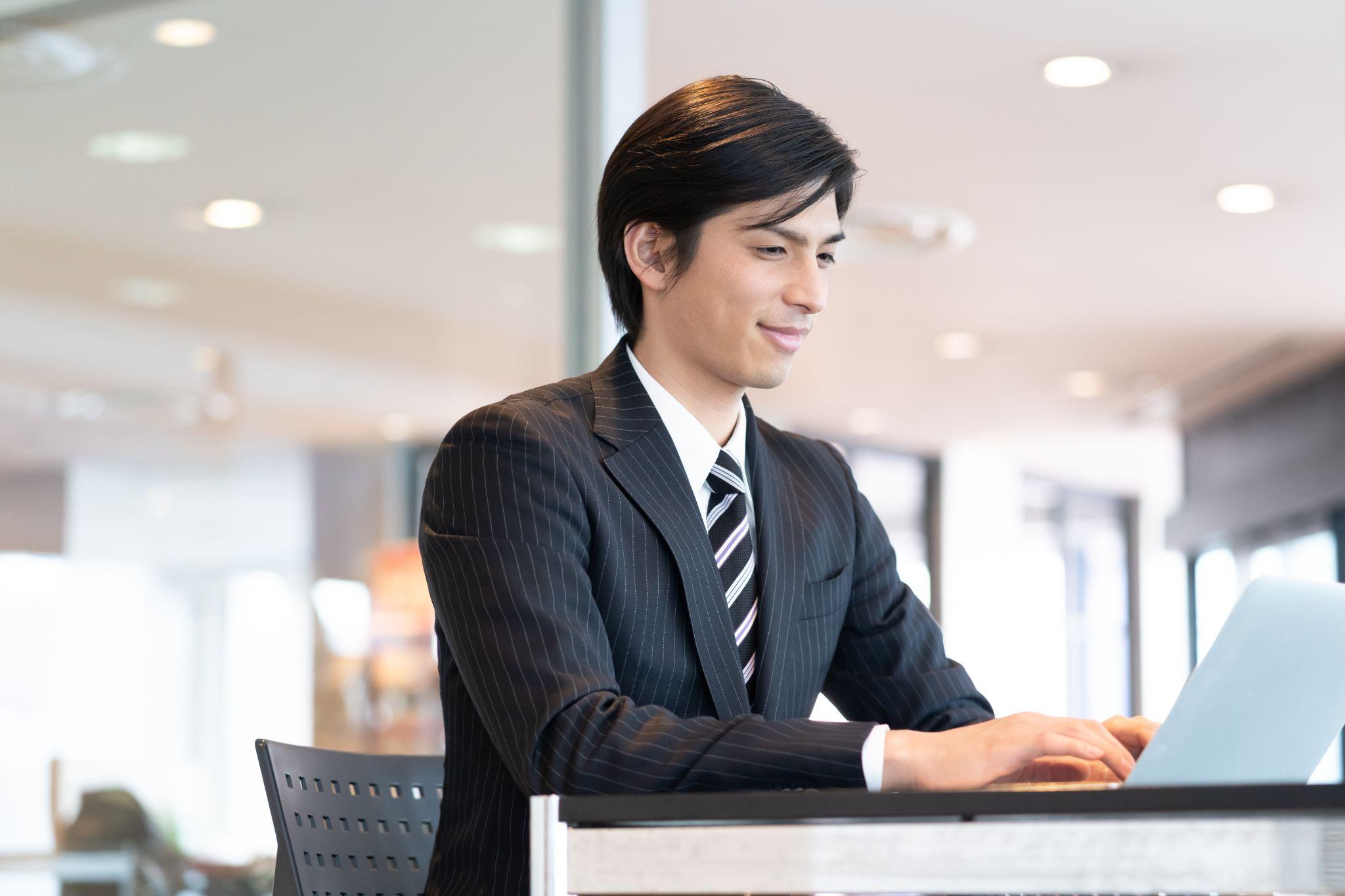 オフィスでノートパソコンを操作し、笑顔を見せるビジネスパーソン