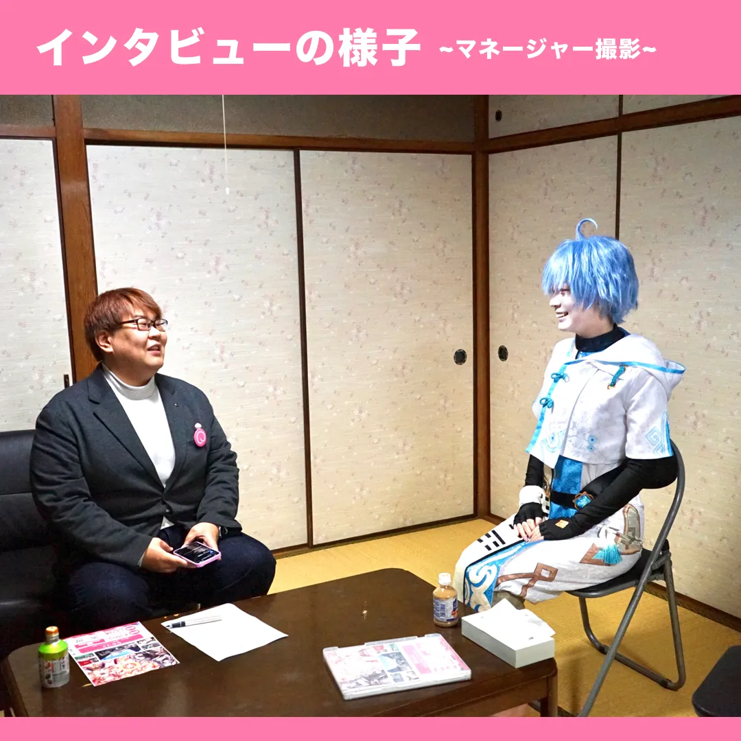 ももコス実行委員会代表りんごさんとのインタビュー風景。和室でりんごさんは青い髪のコスプレ姿、私はスーツ姿で向かい合って談笑している様子。テーブルには取材資料が置かれている。