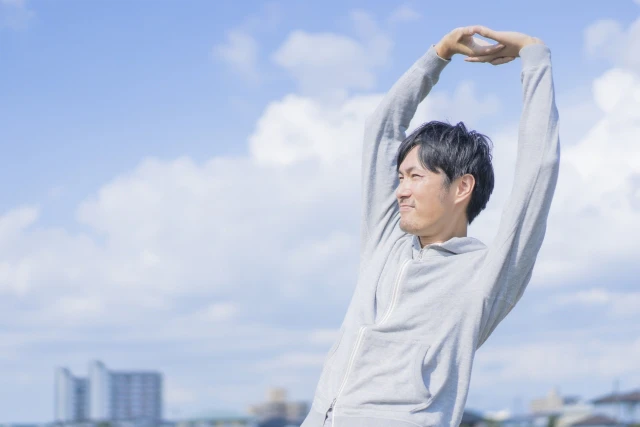 青空の下で伸び伸びとする男性