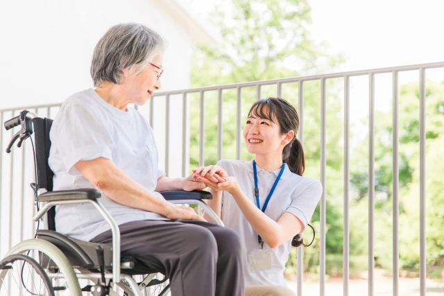 車椅子の女性の手を包み込む看護師さん