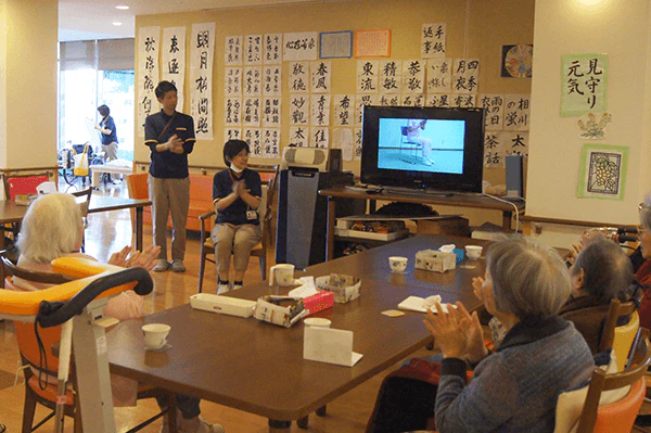 ケアネット徳洲会にてテレビを見る利用者さんと介護職員さん