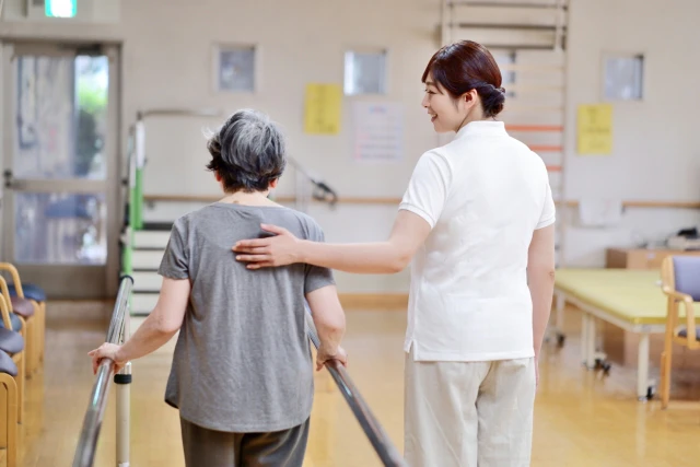 歩行訓練をする女性と支えるスタッフさんの後ろ姿