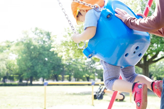 大人にブランコを押してもらって遊ぶ園児