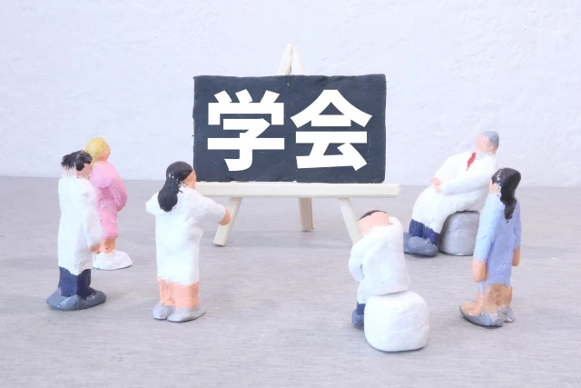 「学会」と書かれた黒板を囲む人形たち