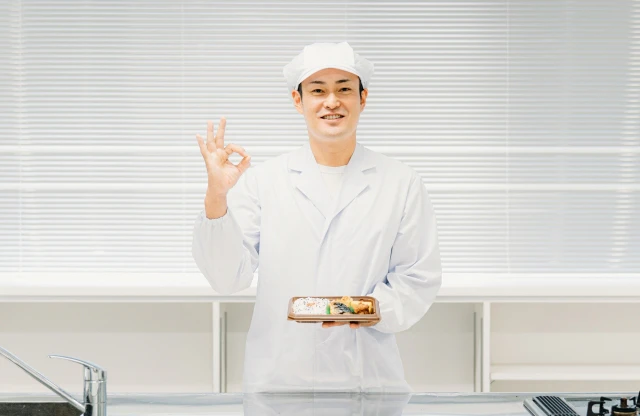 調理室でお弁当を持ちながらgoodサインをする男性