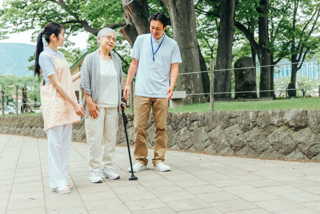 杖をつく年配女性と二人のスタッフ