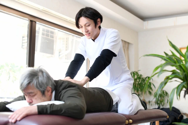男性の背中をもみほぐすスタッフさん