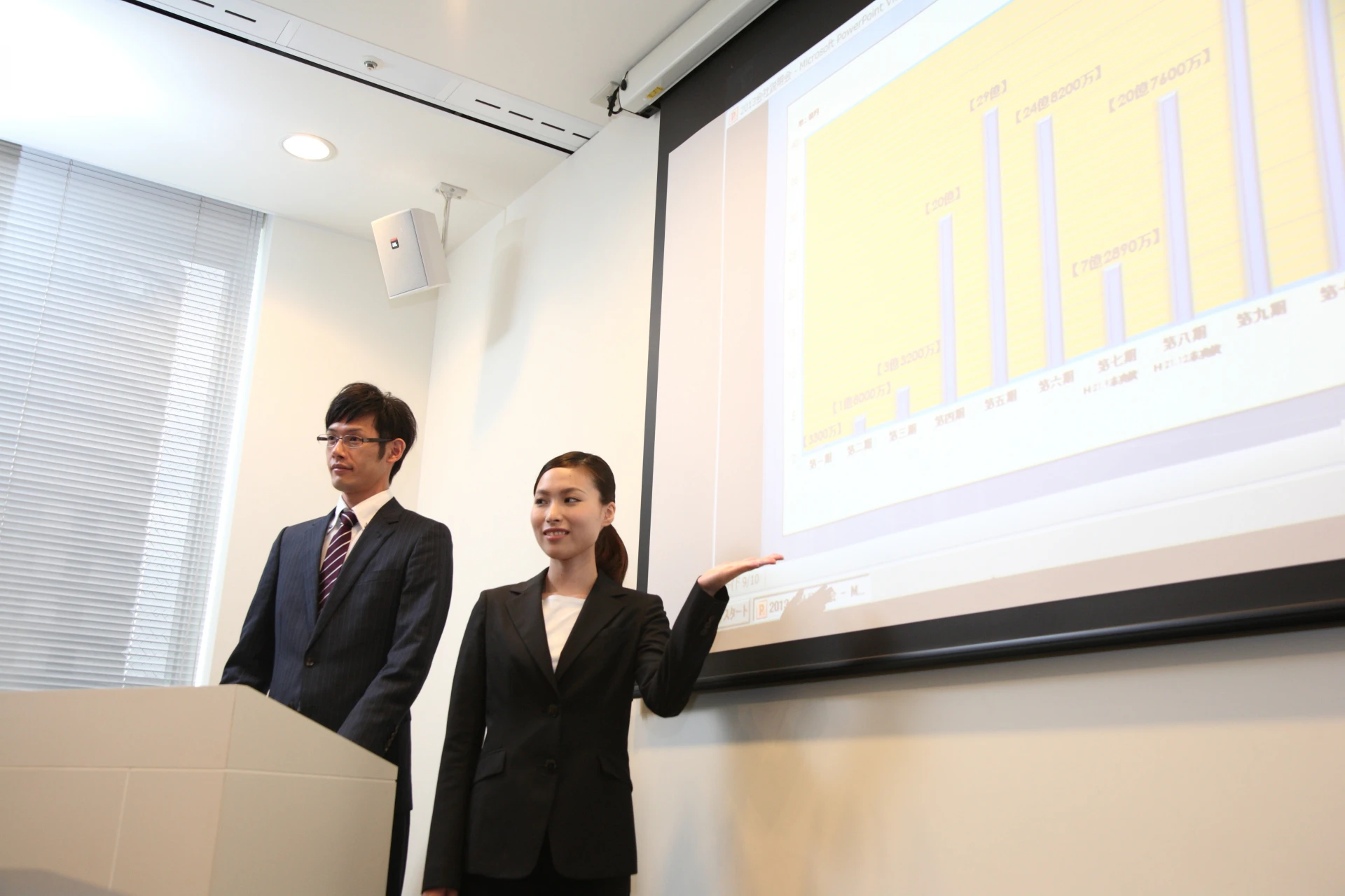 スーツの女性　スクリーン前で解説