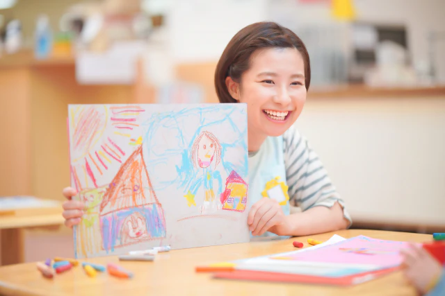 園児が描いた絵を笑顔で持つ女性