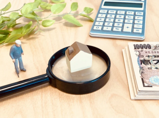 虫眼鏡の上にミニチュアの家とそれを見ている高齢男性の人形