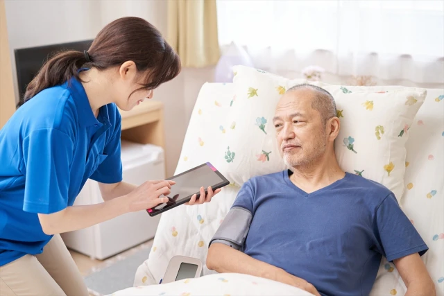 療養中の男性の血圧を測るスタッフ