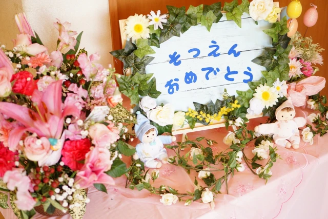 「そつえんおめでとう」と書かれたボードと花と人形