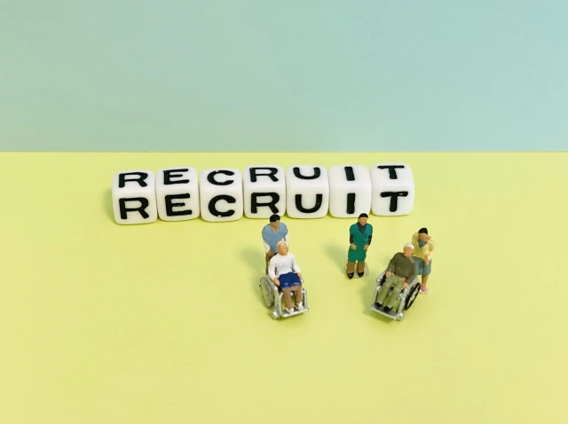 「RECRUIT」の文字とミニチュアのスタッフと車椅子の男性