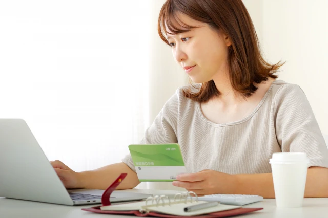 通帳を見ながらパソコン作業をする女性