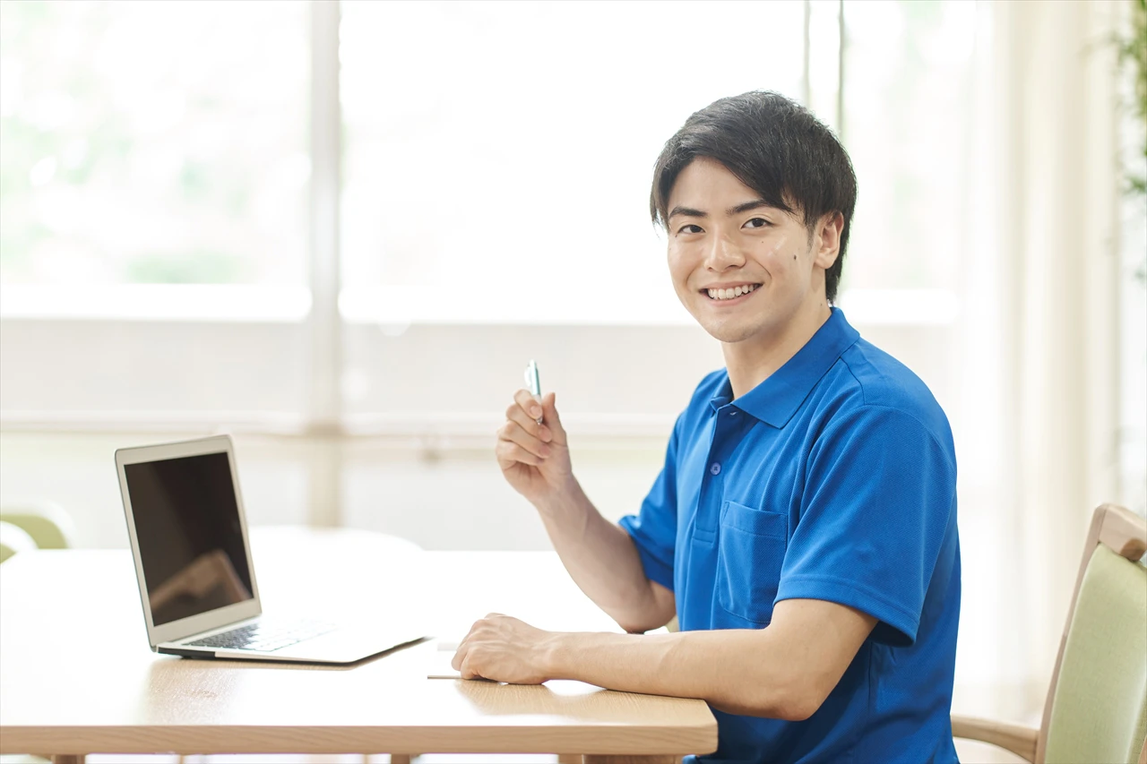 パソコンの前でボールペンを片手に笑顔のケースワーカーさん