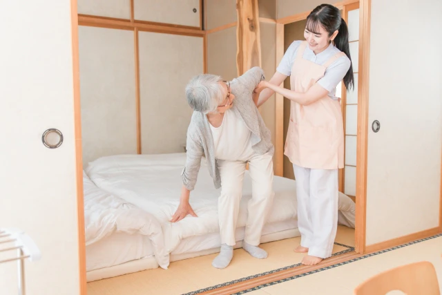 立ち上がるのを介助してもらう年配女性とスタッフ