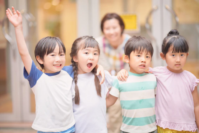 子ども4人が肩を組んでいる姿を保育士が見守っている様子