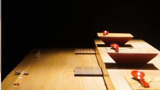 鮨おくむらの店内。白木のカウンターに朱の器が並ぶ設え