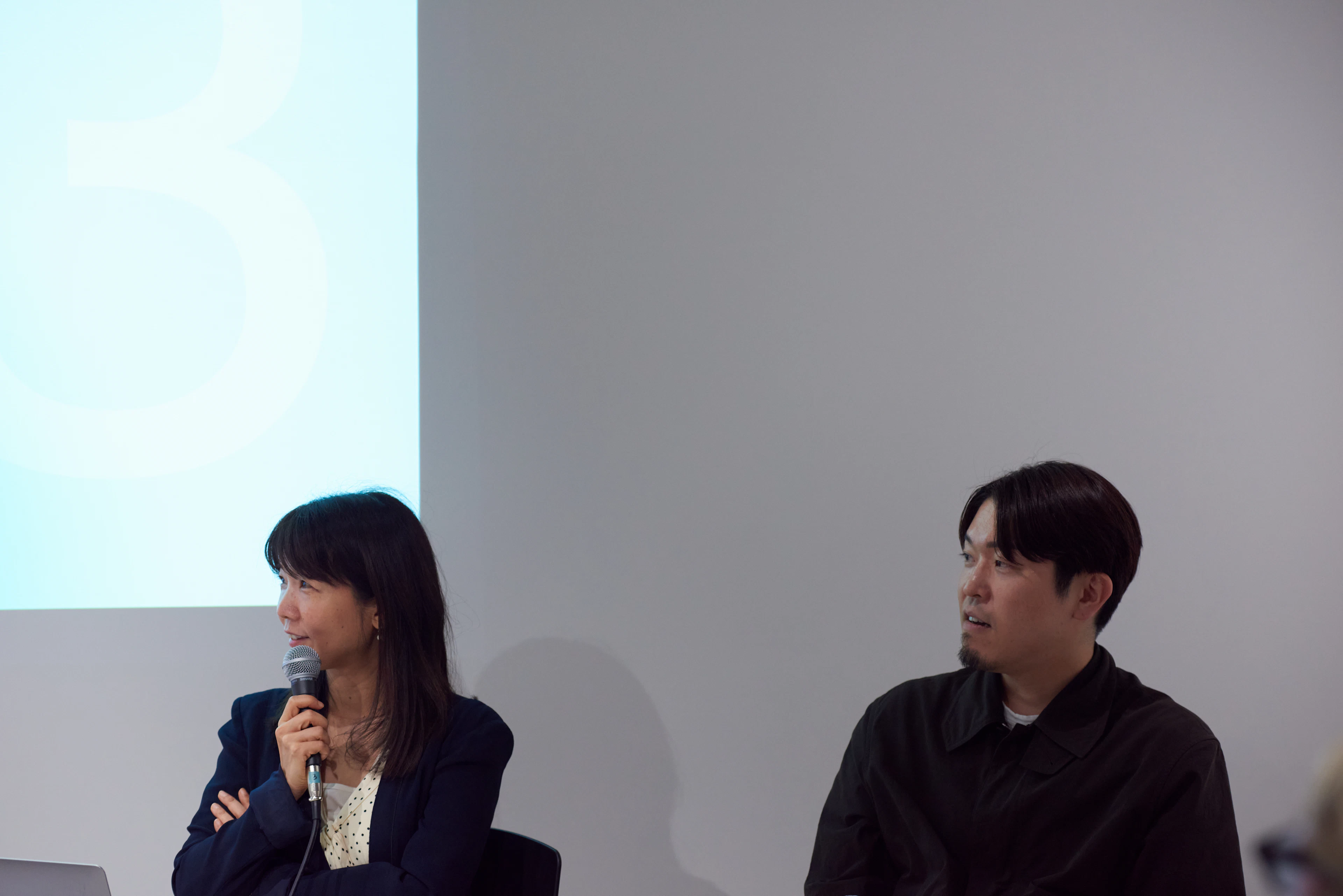 柳澤田実さんがマイクで発言し、隣で安斎勇樹さんが話に耳を傾けている様子