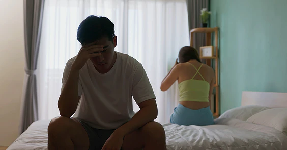 ベッドに座って悩みを抱えている男性のイメージ