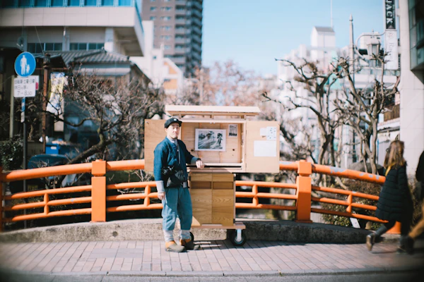 橋のたもとで移動式の展示什器を引く人
