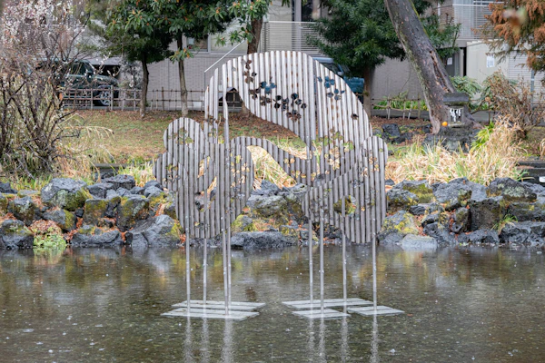 池のほとりに立つ、細い棒を並べてつくられた立体作品