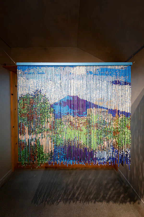 ビーズを連ねてつくられた、山と草木の風景ののれん状の作品